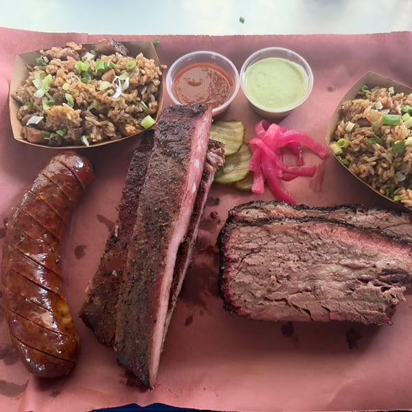 Smoky Buns BBQ platter with sliced brisket, ribs, sausage, dirty rice, pickles, and sauces.
