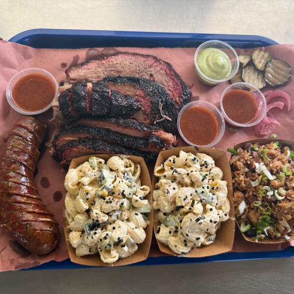 Smoky Buns BBQ platter with sliced brisket, sausage, macaroni salad, fried rice, and sauces.