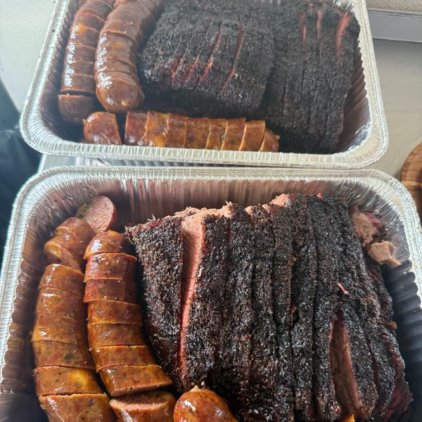 Two foil pans filled with sliced smoked brisket and sausage from Smoky Buns.