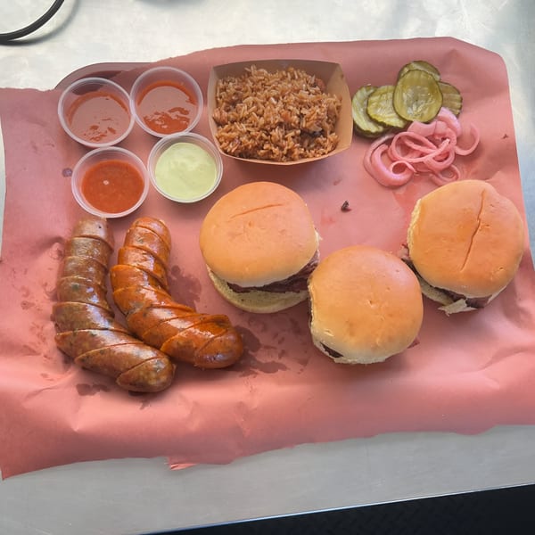 Smoky Buns BBQ platter with sliced sausage, sliders, rice, pickles, pickled onions, and sauces.