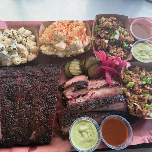 Smoky Buns' BBQ platter with ribs, brisket, macaroni salad, potato salad, dirty rice, pickles, and sauces.