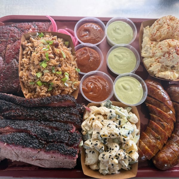 A BBQ platter with brisket, ribs, sausage, rice, potato salad, macaroni salad, and sauces.