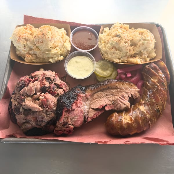 Smoky Buns BBQ platter with pulled pork, sliced brisket, sausage, potato salad, and sauces.